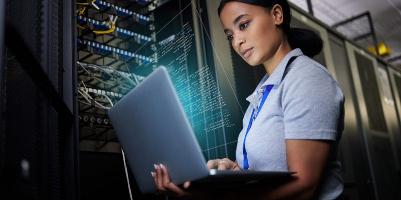 Digitale Infrastruktur im Rechenzentrum IT-Spezialistin arbeitet an einem Laptop in einem modernen Rechenzentrum mit vernetzten Servern – Symbol für digitale Infrastruktur und Netzwerkmanagement.